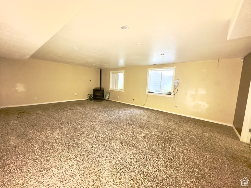 Empty room with a wood stove, baseboards, and carpet