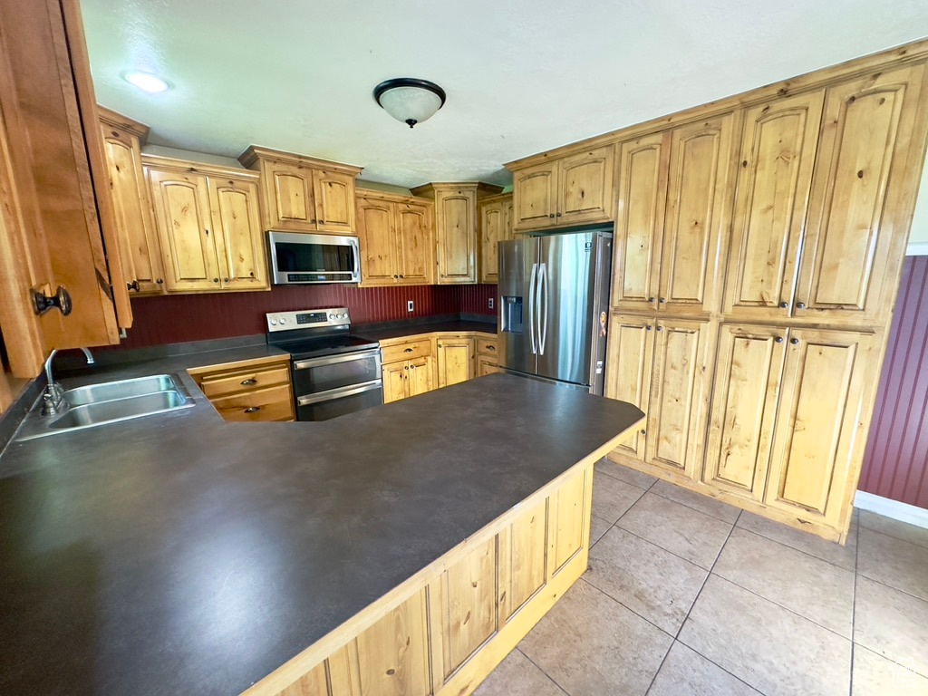 Kitchen featuring appliances with stainless steel finishes, a sink, dark countertops, and light tile patterned floors