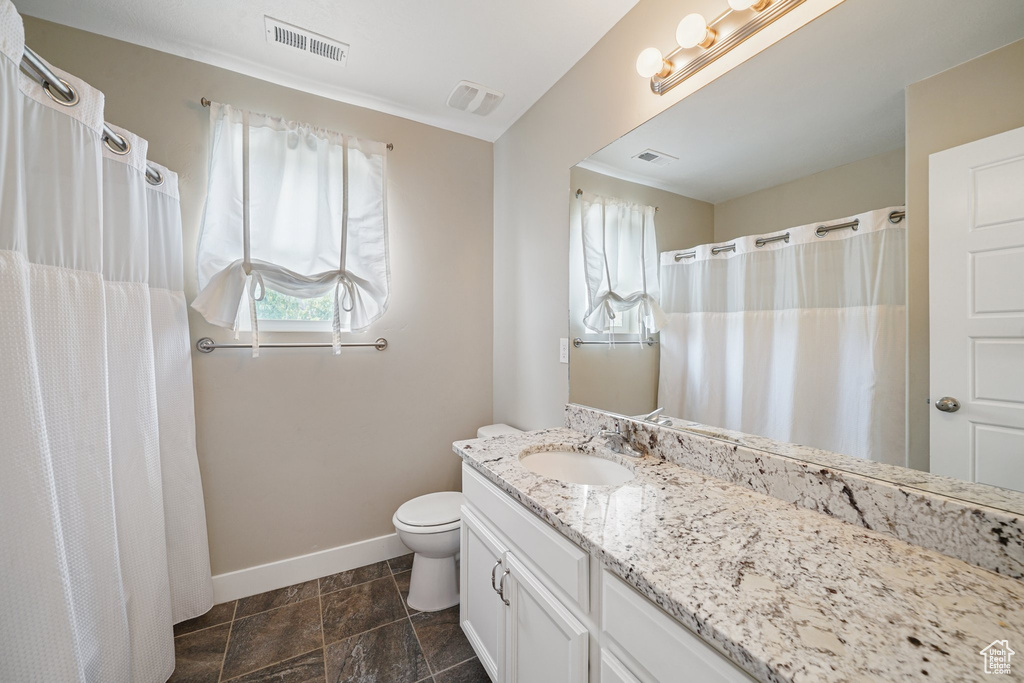 Bathroom featuring baseboards, vanity, toilet, and stone finish floors