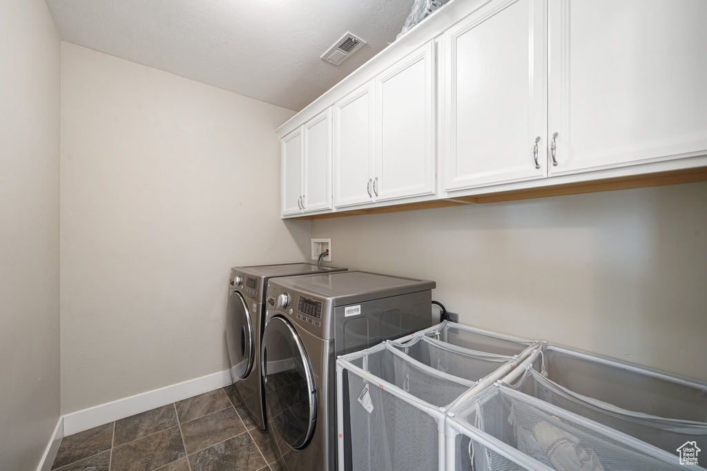 Laundry area featuring cabinet space, baseboards, separate washer and dryer, and dark stone finish flooring
