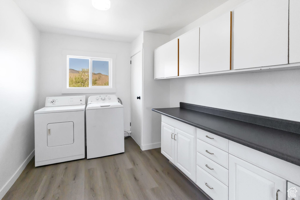 Washroom featuring washing machine and clothes dryer, light wood-type flooring, cabinet space, and baseboards