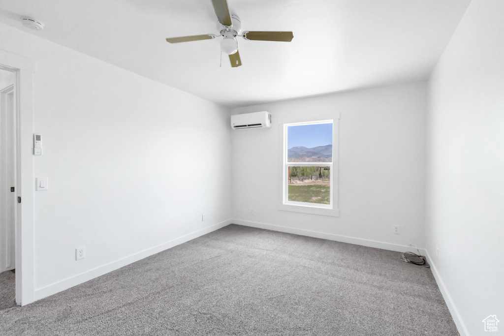 Unfurnished room with a wall unit AC, carpet flooring, a smoke detector, and a ceiling fan