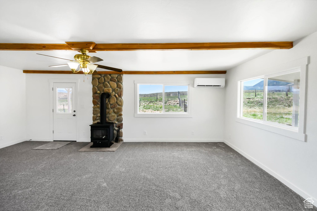 Unfurnished living room featuring beam ceiling, a wall mounted air conditioner, a wood stove, carpet floors, and baseboards