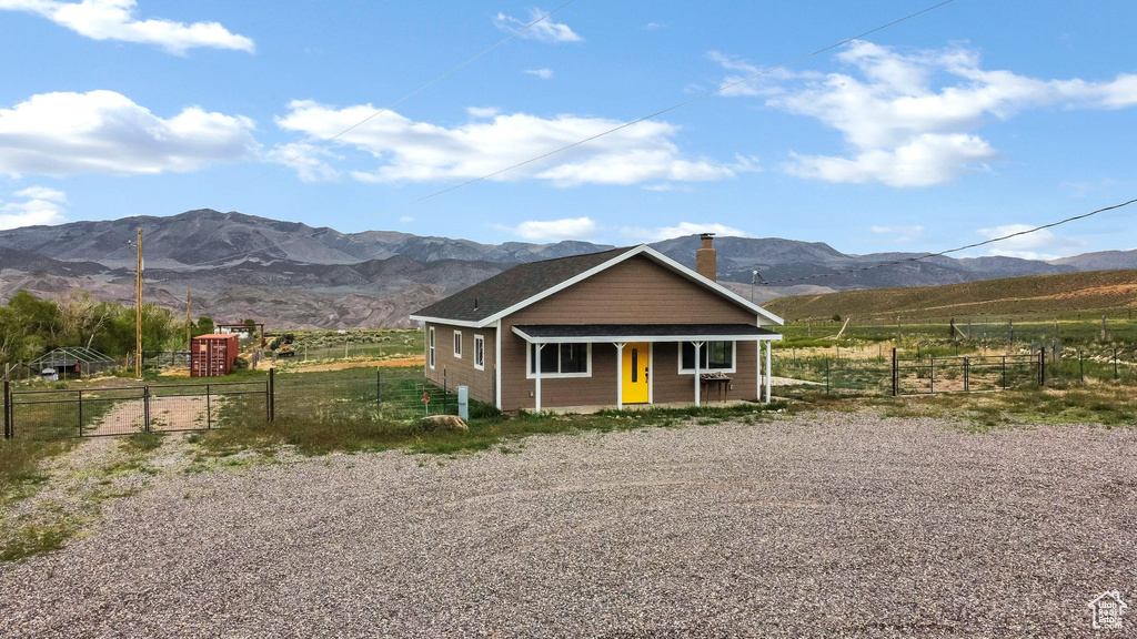 View of front of home with a mountain view, fence, covered porch, a chimney, and a rural view