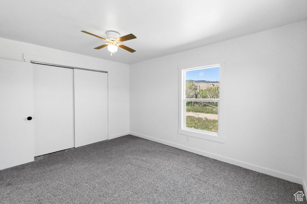 Unfurnished bedroom with dark colored carpet, a closet, a ceiling fan, and baseboards
