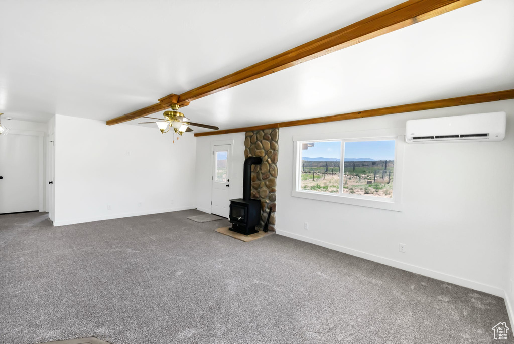 Unfurnished living room featuring a wall mounted AC, a wood stove, carpet flooring, and baseboards