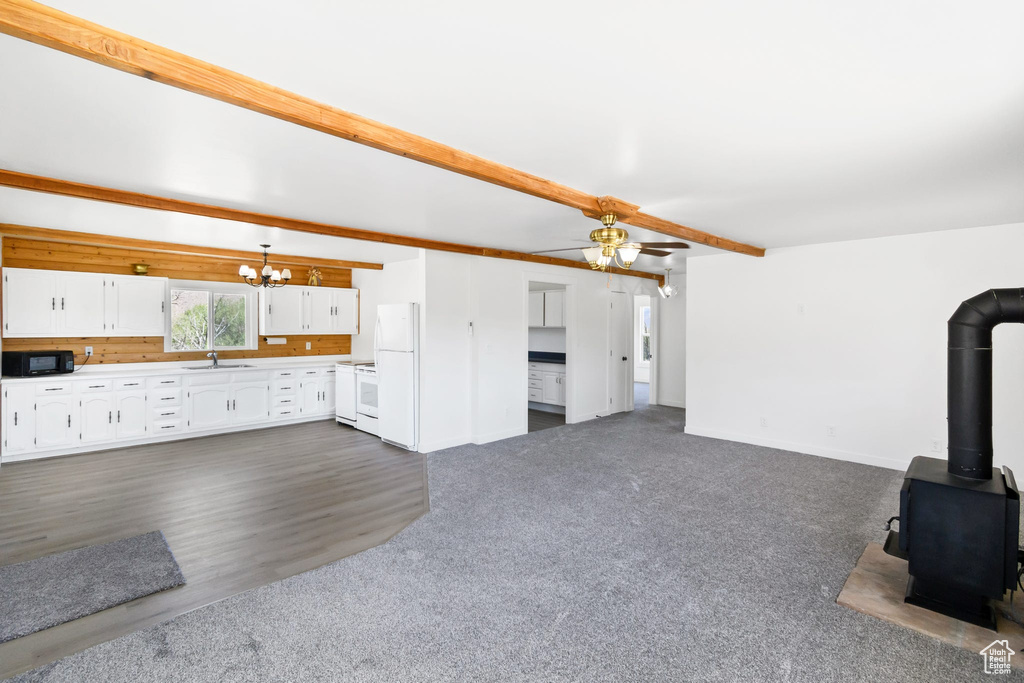 Unfurnished living room with a chandelier, a ceiling fan, a wood stove, baseboards, and beam ceiling