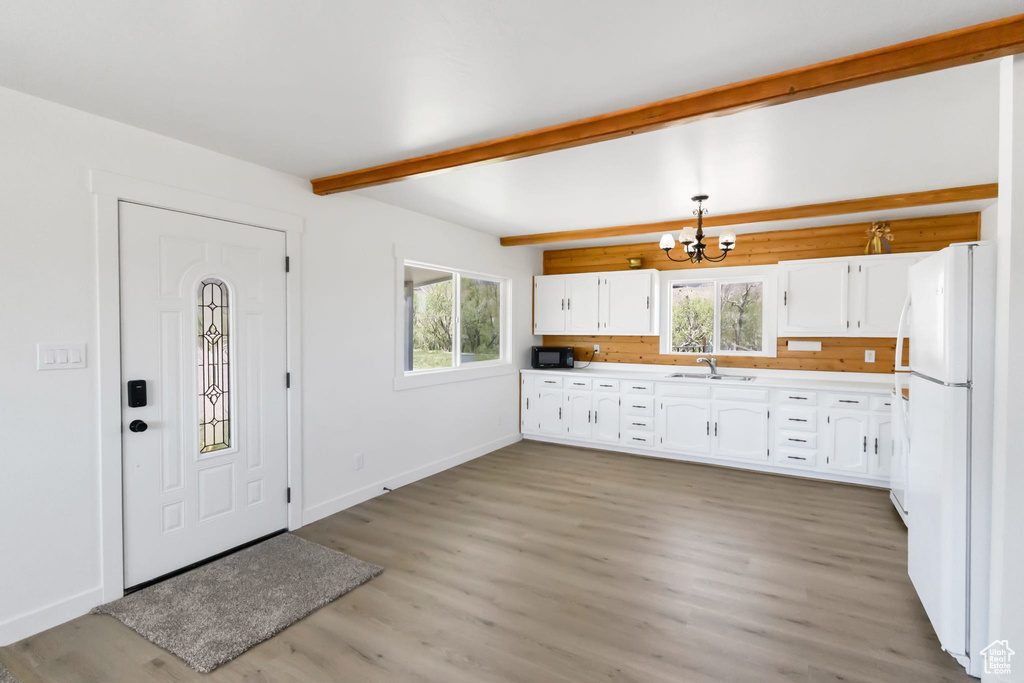 Kitchen featuring a sink, freestanding refrigerator, a chandelier, beam ceiling, and white cabinets