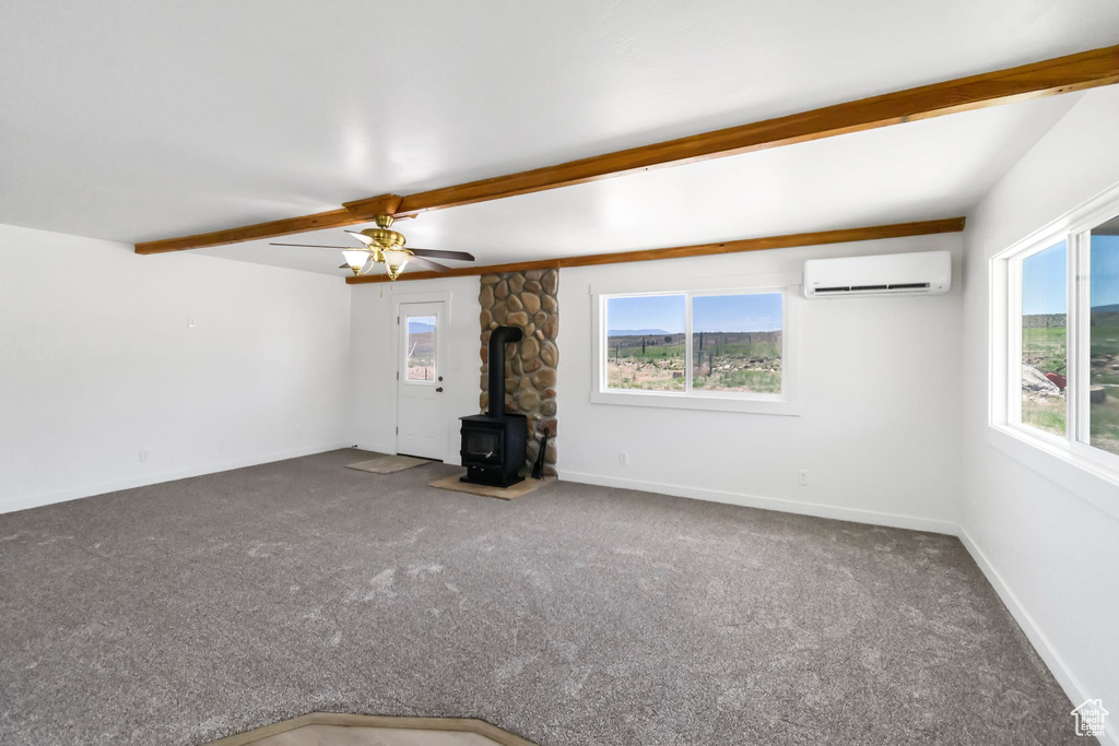 Unfurnished living room featuring a wood stove, an AC wall unit, carpet flooring, and baseboards