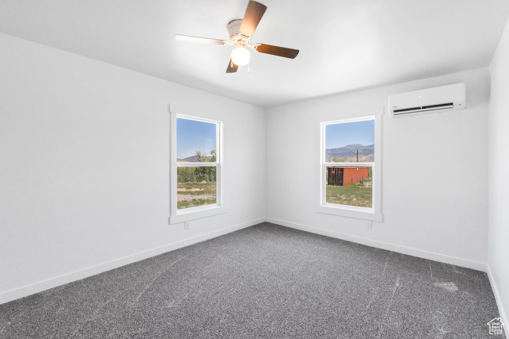 Unfurnished room featuring an AC wall unit, dark colored carpet, baseboards, and a ceiling fan