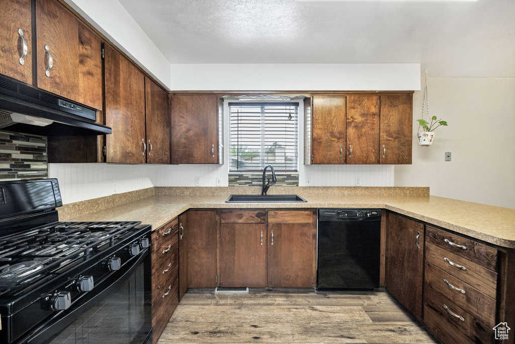 Kitchen featuring black appliances, a sink, under cabinet range hood, light wood finished floors, and light countertops