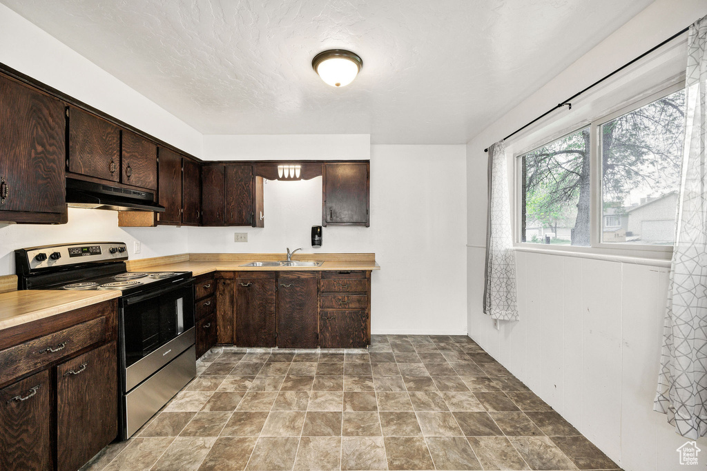 Kitchen with stainless steel electric range oven, under cabinet range hood, a sink, light countertops, and dark brown cabinets