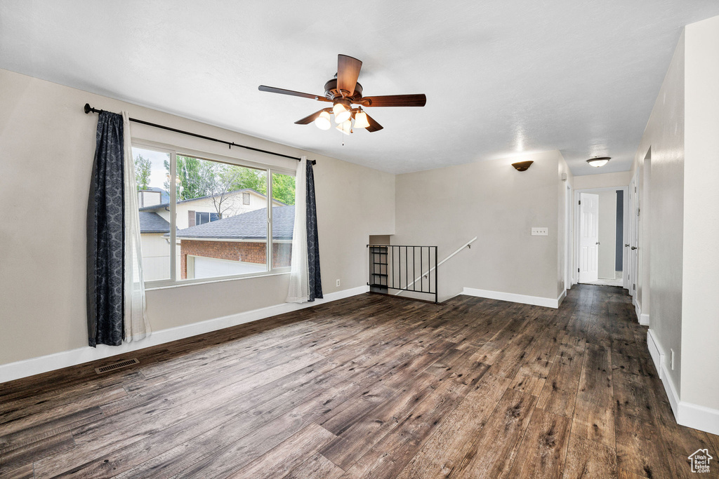 Empty room featuring dark wood-type flooring, a ceiling fan, and baseboards