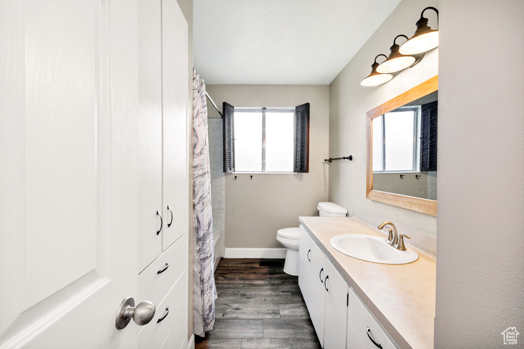 Bathroom with wood finished floors, toilet, vanity, baseboards, and a shower with shower curtain
