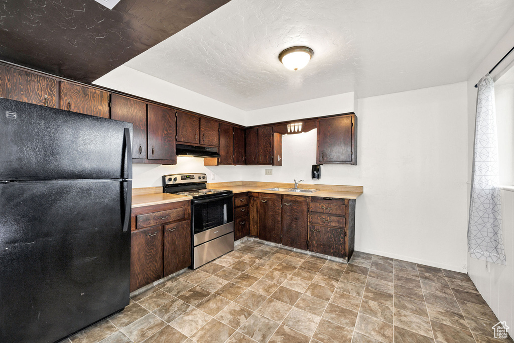 Kitchen featuring freestanding refrigerator, stainless steel electric stove, under cabinet range hood, a sink, and light countertops