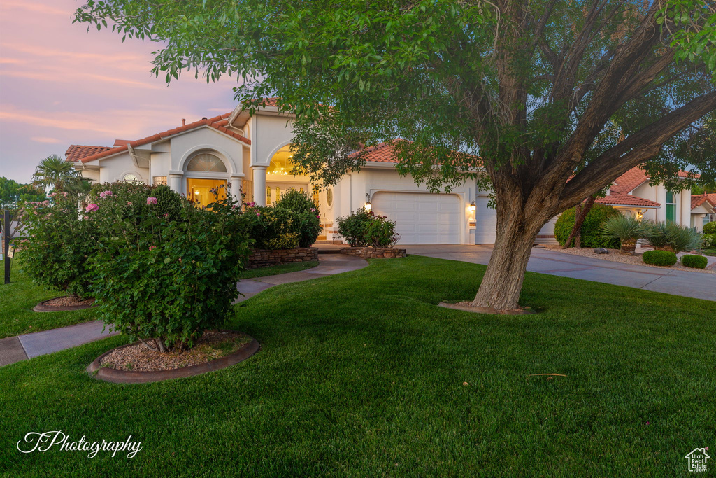Mediterranean / spanish house featuring stucco siding, a tiled roof, concrete driveway, a garage, and a front yard