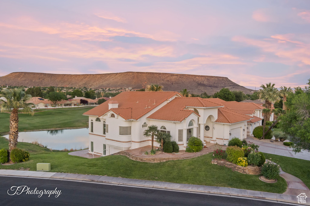 Mediterranean / spanish-style house with a water and mountain view, a front lawn, a garage, and stucco siding