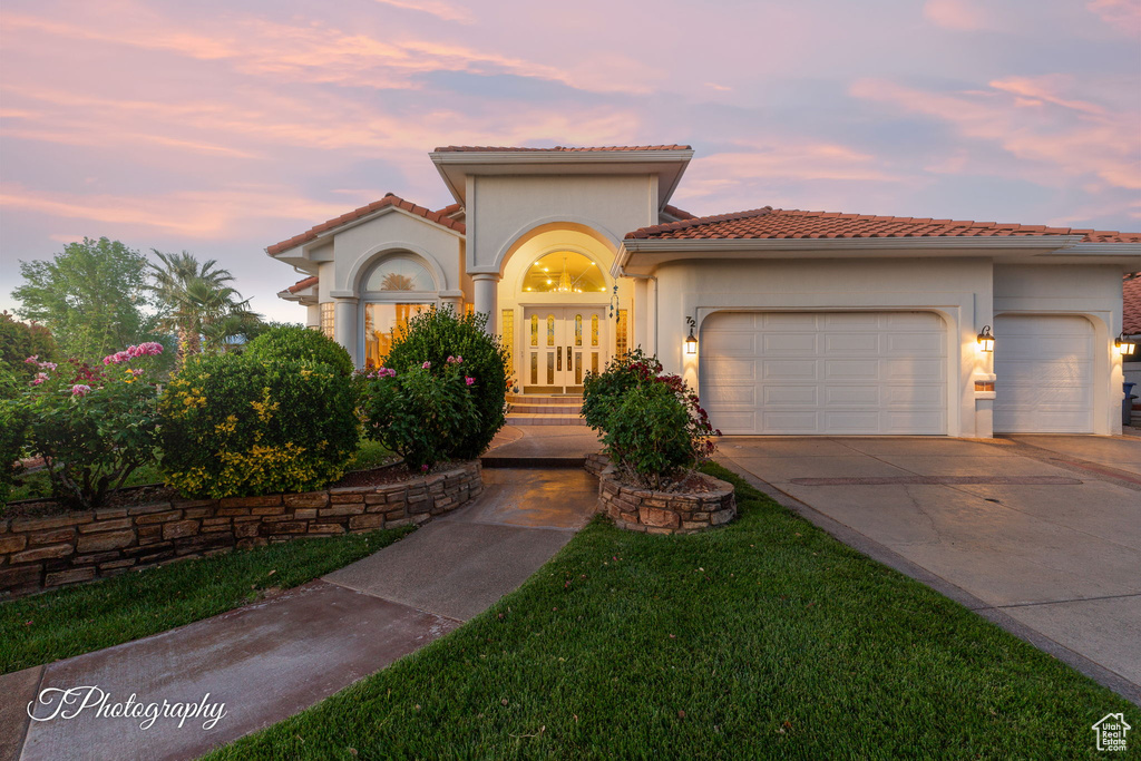 Mediterranean / spanish house featuring an attached garage, a tiled roof, concrete driveway, and stucco siding