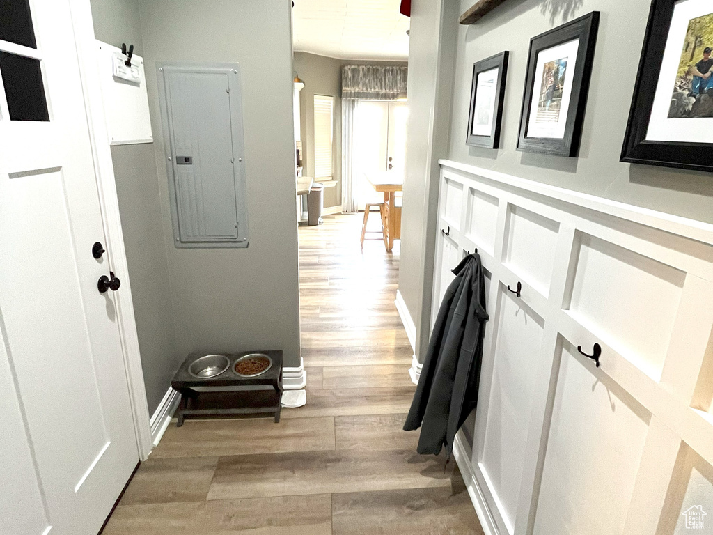 Corridor featuring arched walkways, electric panel, light wood-style floors, and baseboards