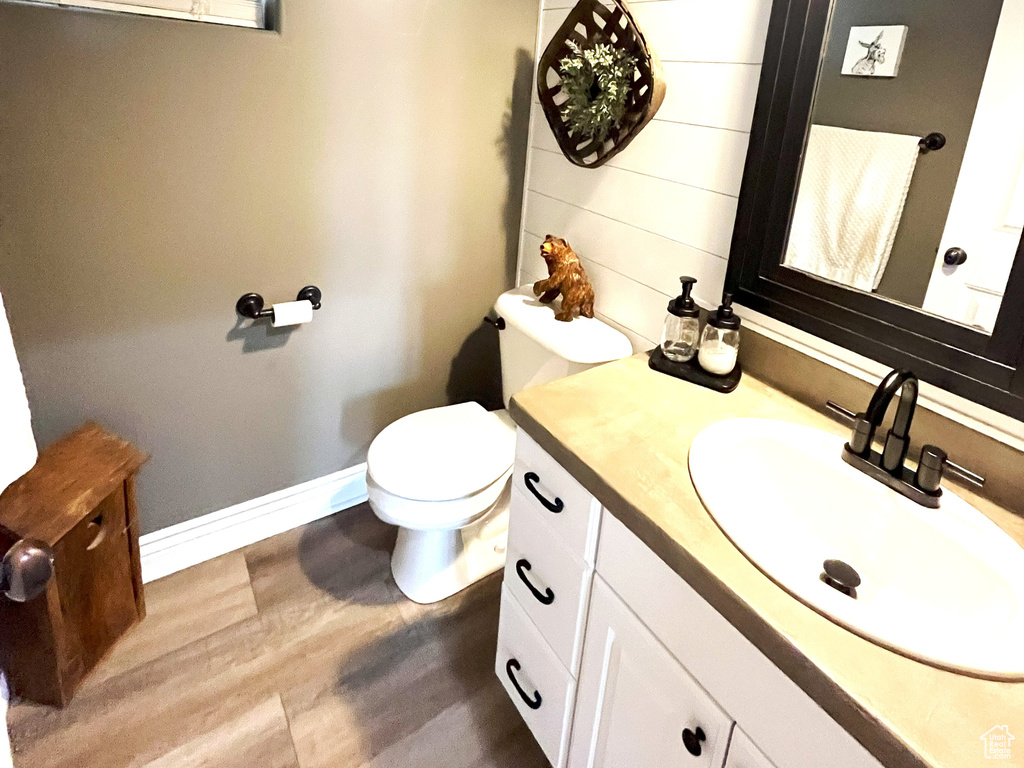 Half bathroom featuring wood finished floors, vanity, toilet, baseboards, and wooden walls