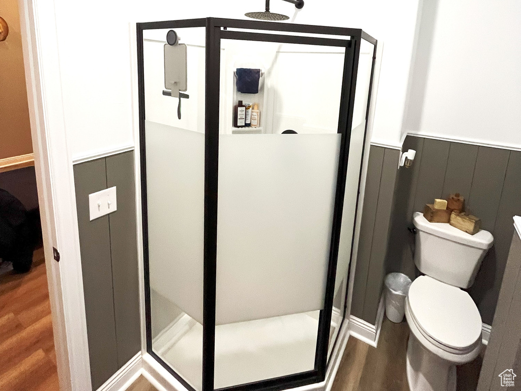Bathroom featuring wood finished floors, wainscoting, a stall shower, and toilet