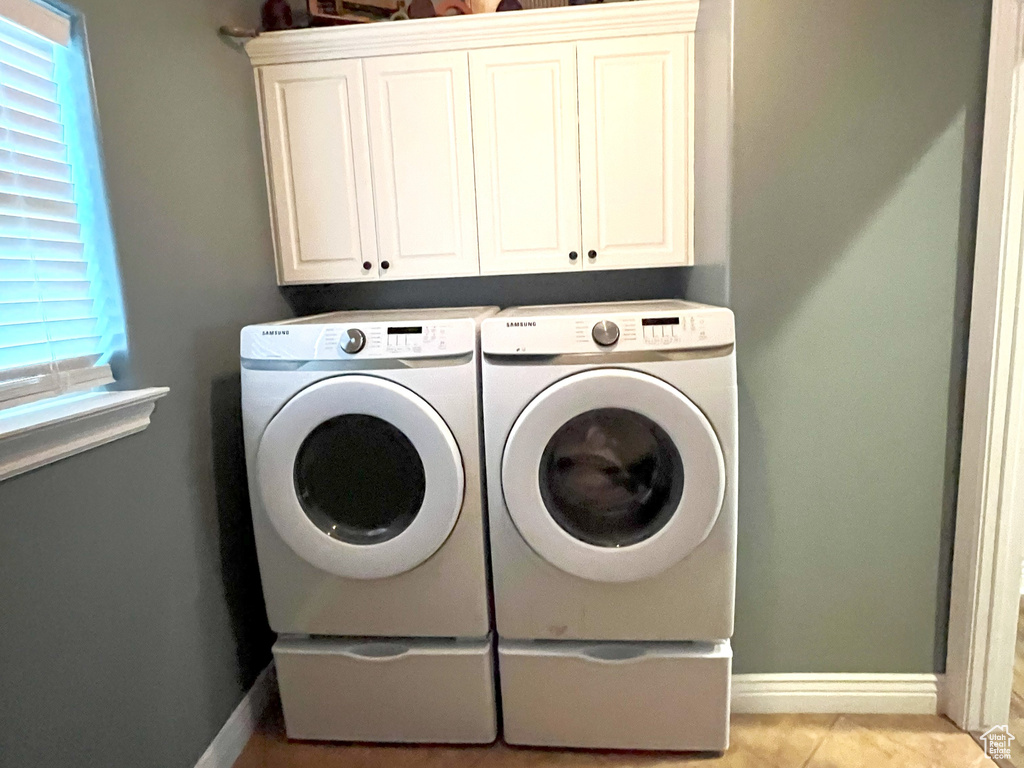 Laundry room with cabinet space, washing machine and clothes dryer, light tile patterned floors, and baseboards
