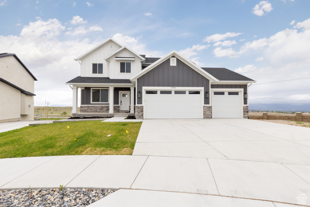 Craftsman-style home featuring an attached garage, board and batten siding, concrete driveway, a front lawn, and stone siding