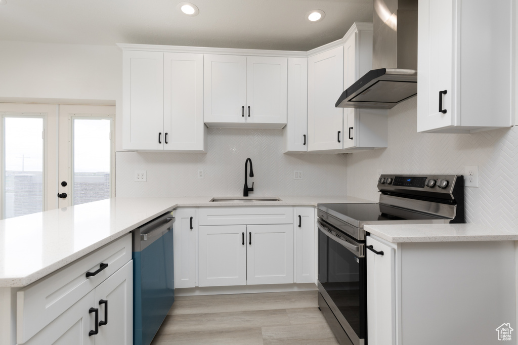 Kitchen with electric range, wall chimney range hood, dishwasher, a sink, and light countertops