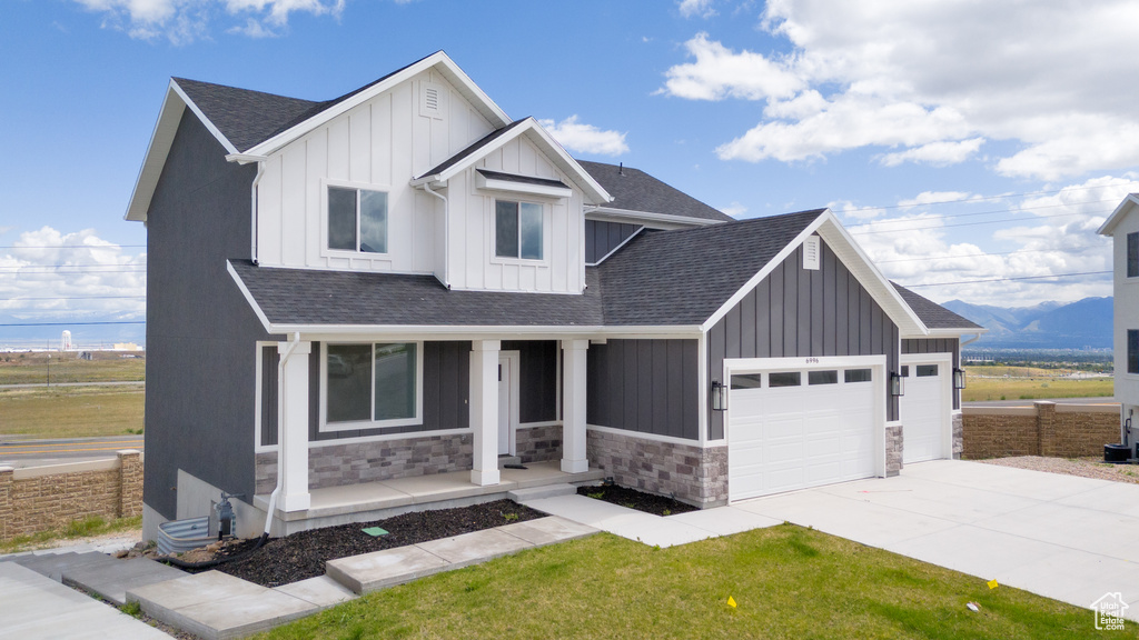Modern inspired farmhouse featuring covered porch, board and batten siding, a garage, and stone siding