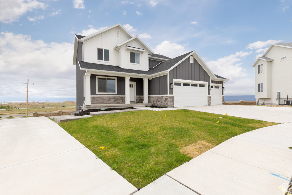 Craftsman-style home with board and batten siding, driveway, a front yard, and stone siding