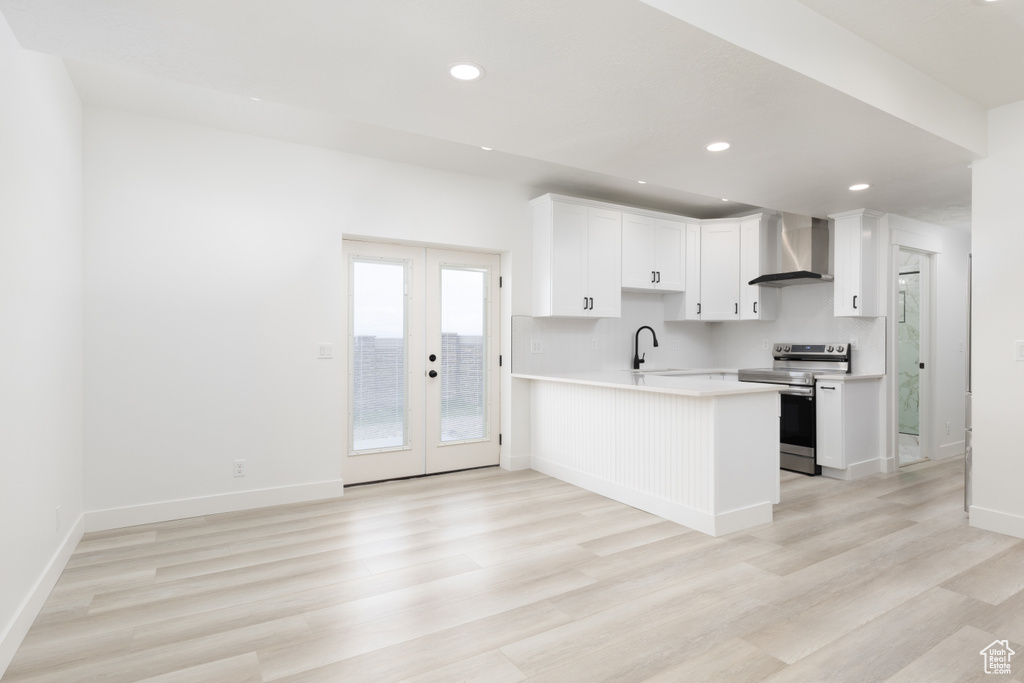 Kitchen featuring stainless steel electric range oven, wall chimney range hood, a peninsula, light countertops, and a sink
