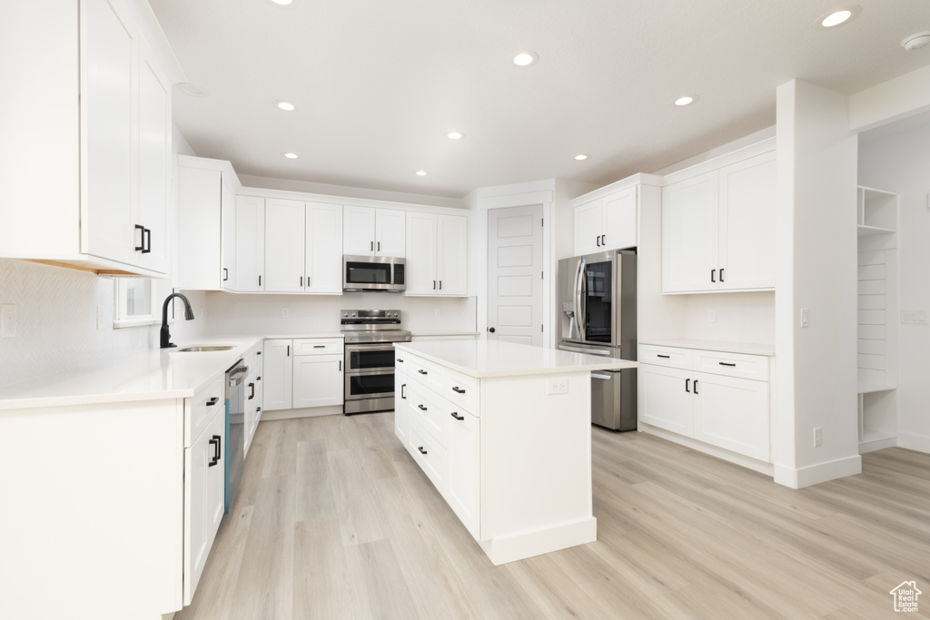 Kitchen with stainless steel appliances, light wood finished floors, recessed lighting, a kitchen island, and light countertops
