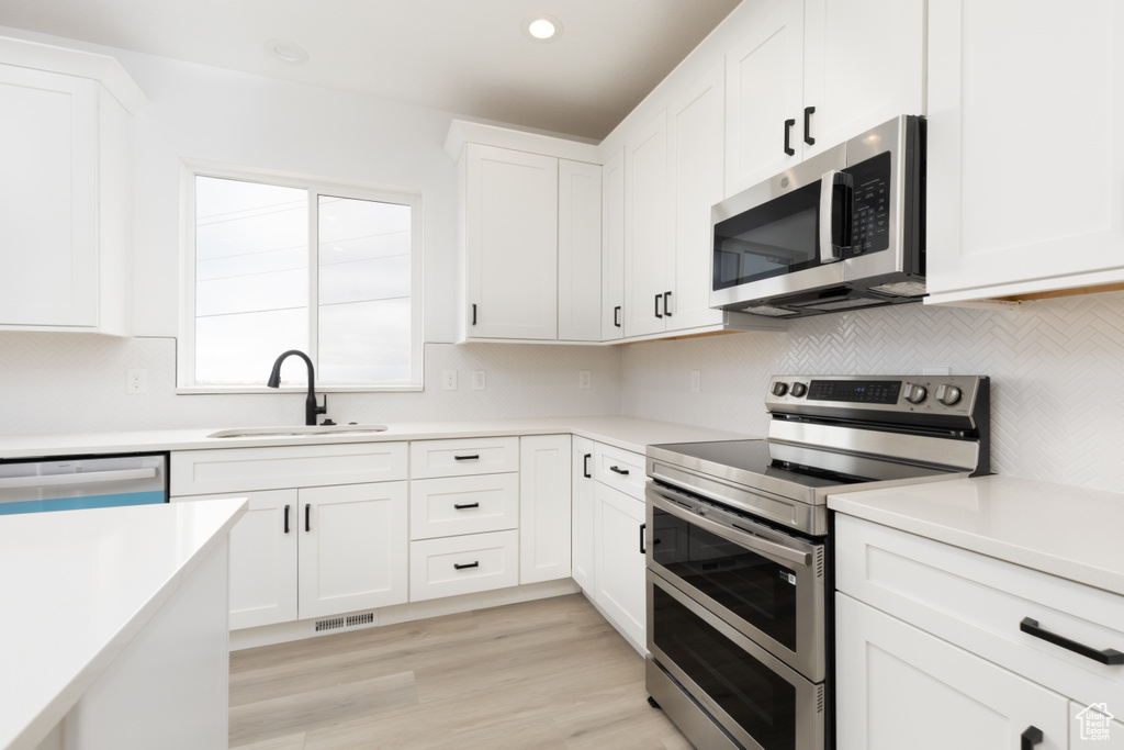 Kitchen featuring appliances with stainless steel finishes, backsplash, light countertops, white cabinets, and recessed lighting