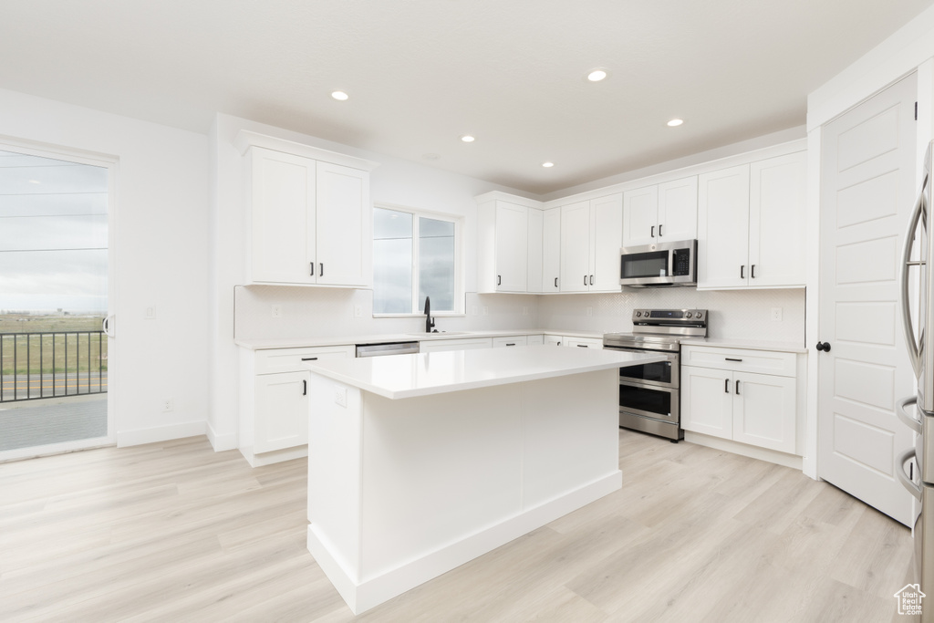 Kitchen featuring appliances with stainless steel finishes, light wood-style floors, light countertops, a center island, and recessed lighting