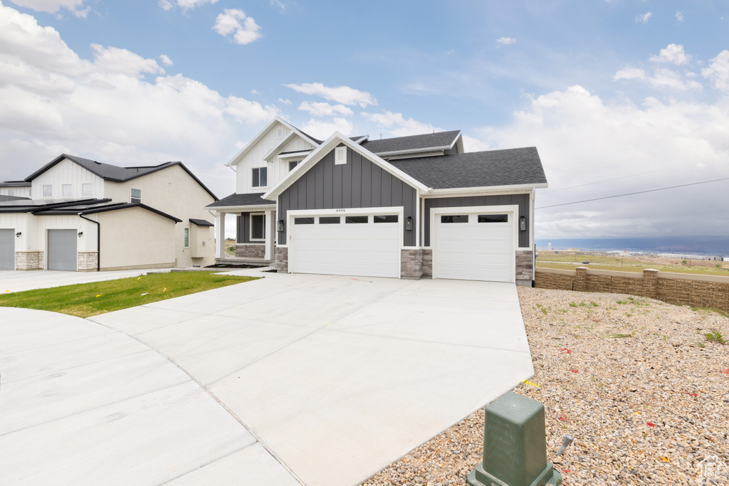 View of front of home with board and batten siding, stone siding, a garage, driveway, and roof with shingles