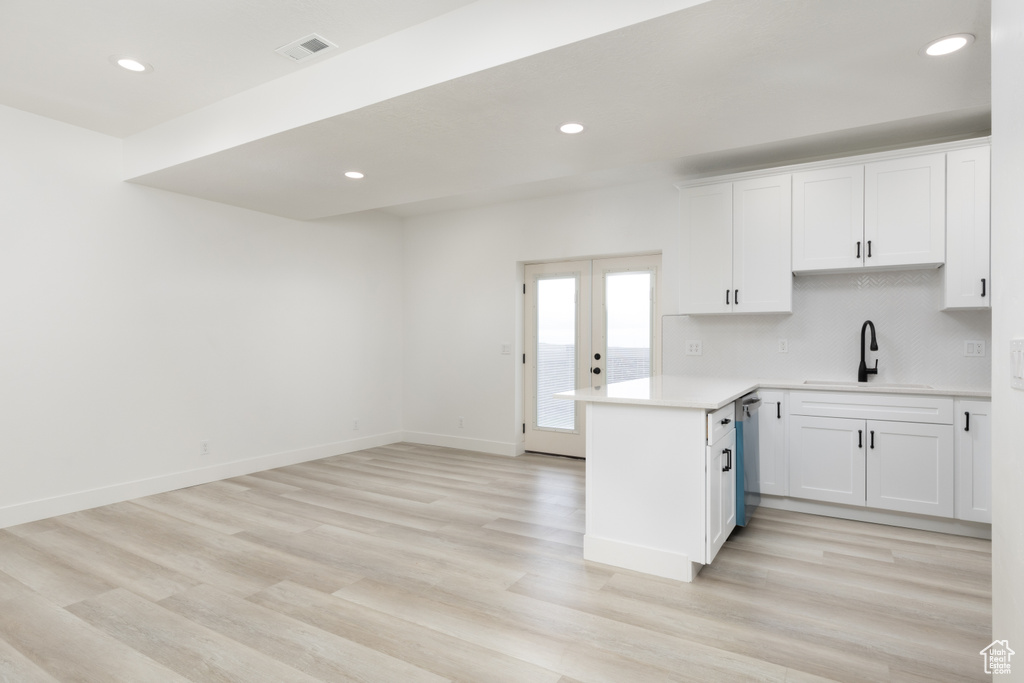 Kitchen with a sink, a peninsula, white cabinets, light countertops, and recessed lighting