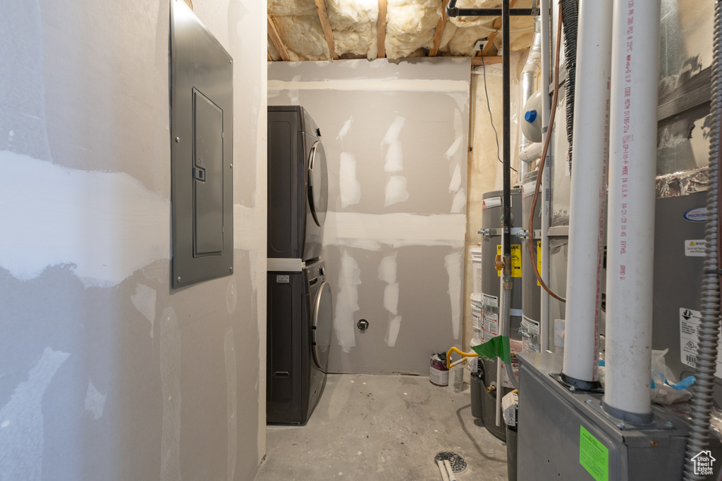 Utility room featuring stacked washer / drying machine, heating unit, and electric panel