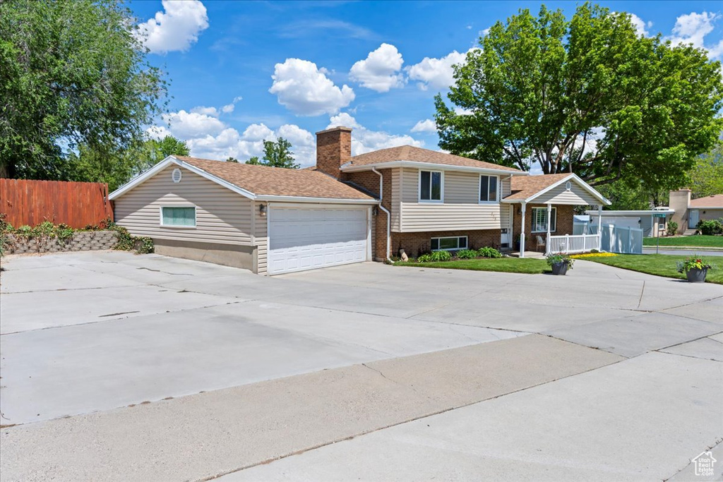 Split level home featuring fence, driveway, a chimney, and an attached garage