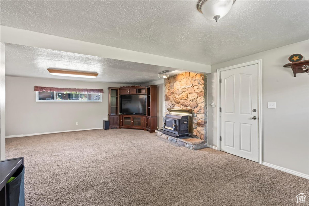 Unfurnished living room featuring a textured ceiling, a wood stove, carpet flooring, and baseboards