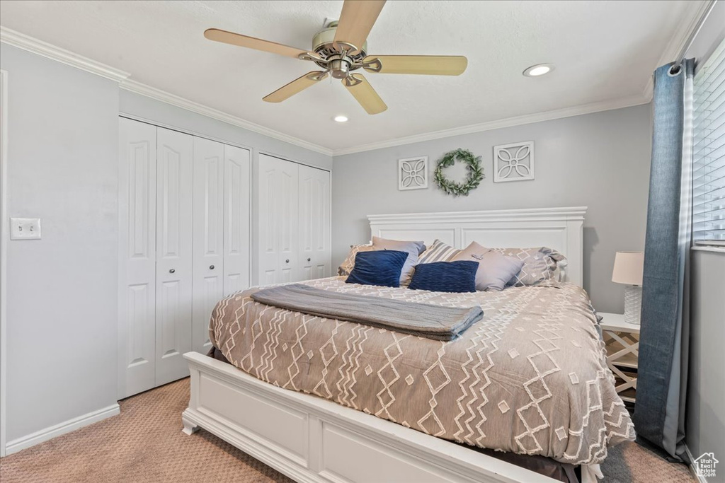 Bedroom with two closets, light carpet, baseboards, recessed lighting, and ornamental molding