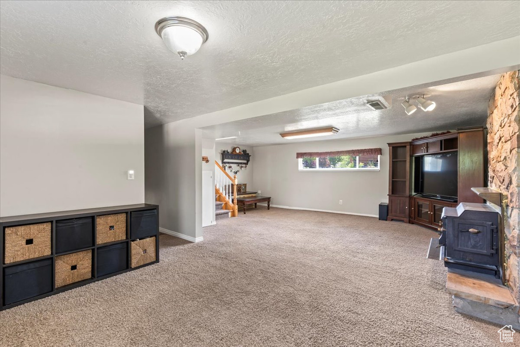 Unfurnished living room with a wood stove, a textured ceiling, carpet flooring, stairway, and baseboards