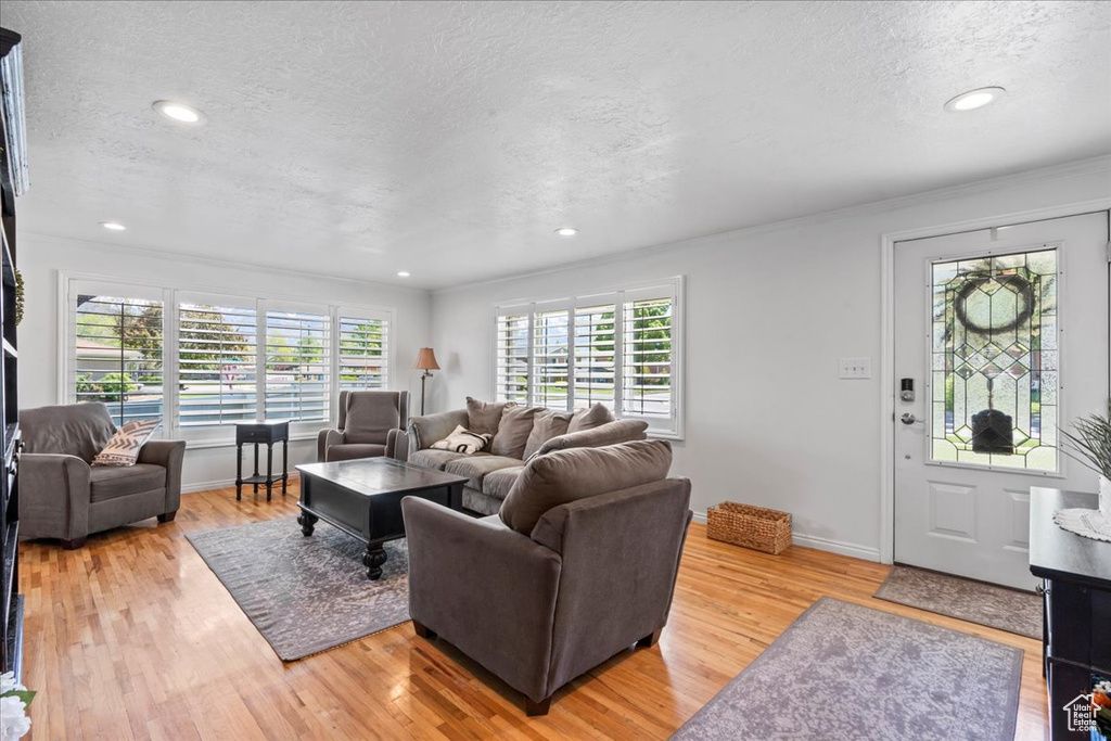 Living room featuring a textured ceiling, light wood-type flooring, recessed lighting, baseboards, and crown molding