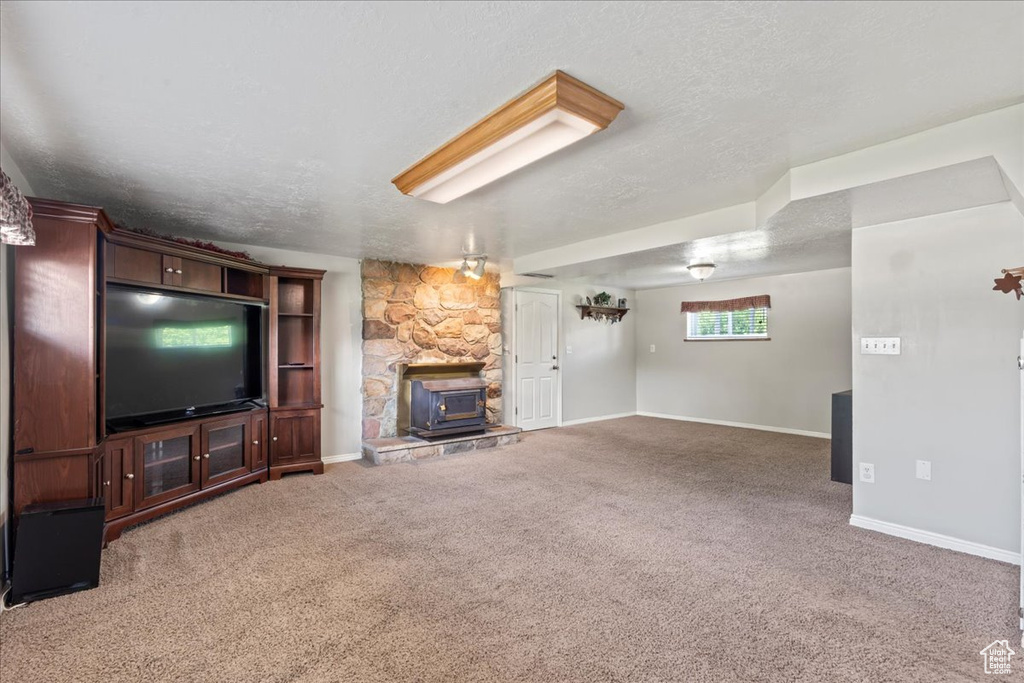 Unfurnished living room featuring a wood stove, baseboards, carpet, and a textured ceiling