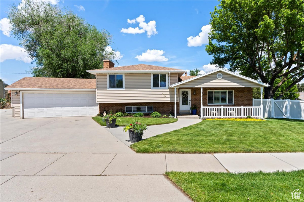 Split level home with brick siding, a garage, covered porch, and a chimney