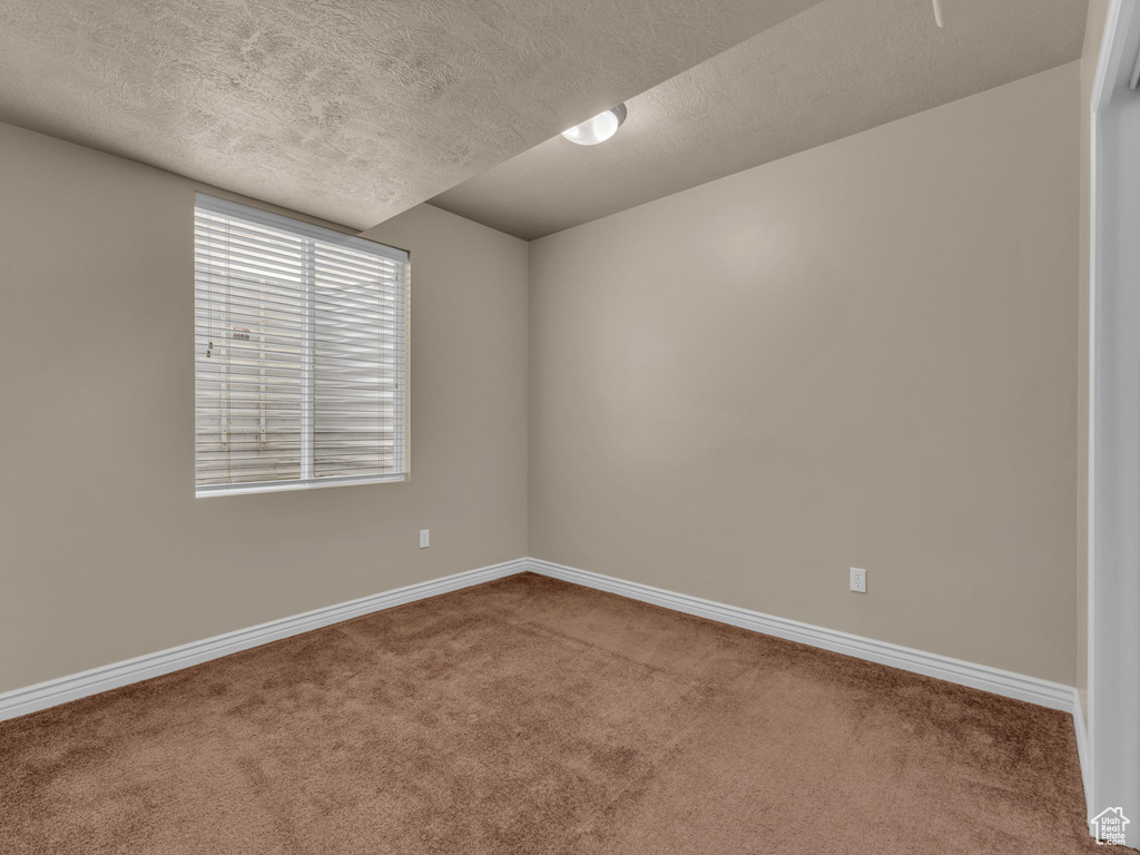Carpeted empty room with a textured ceiling and baseboards