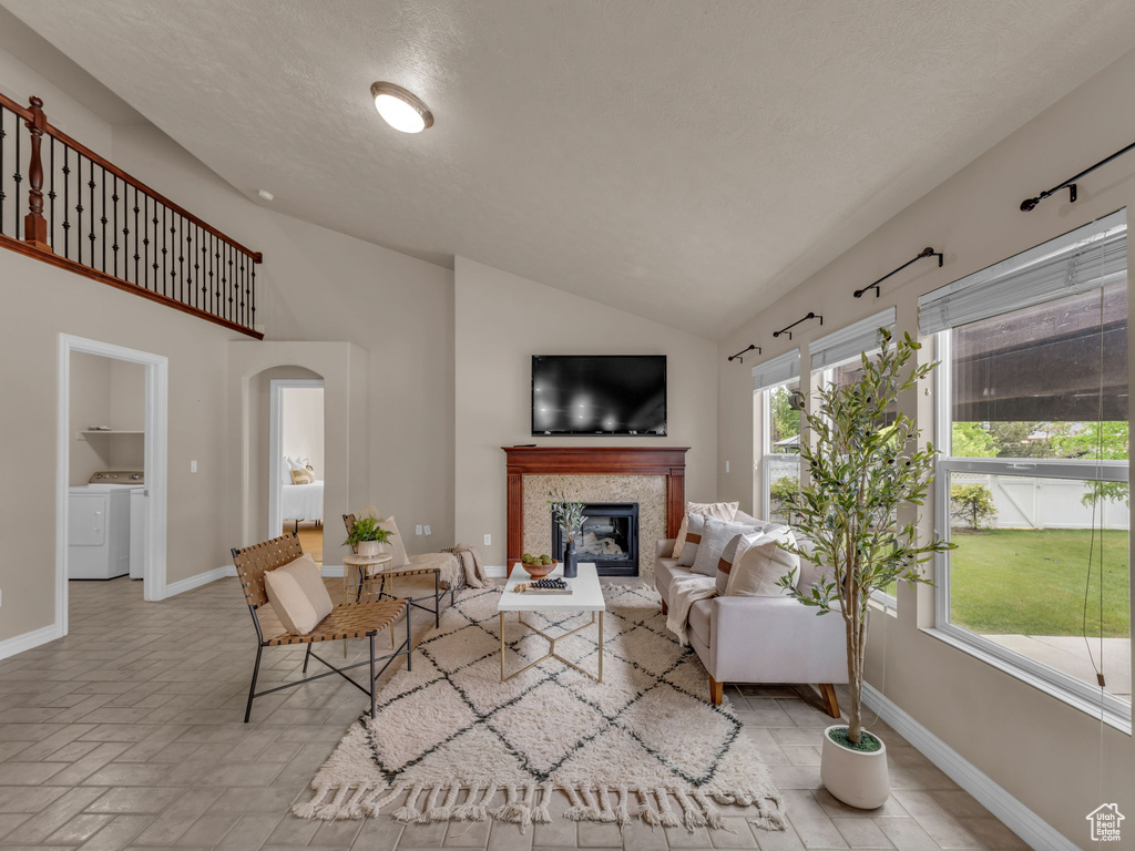 Living room featuring baseboards, a glass covered fireplace, separate washer and dryer, high vaulted ceiling, and arched walkways