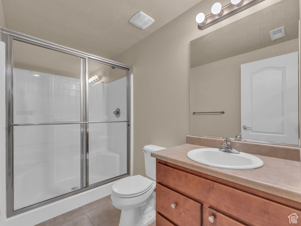 Full bath featuring tile patterned floors, a shower stall, toilet, vanity, and a textured ceiling