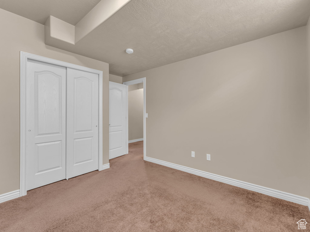 Unfurnished bedroom with carpet flooring, baseboards, a closet, and a textured ceiling