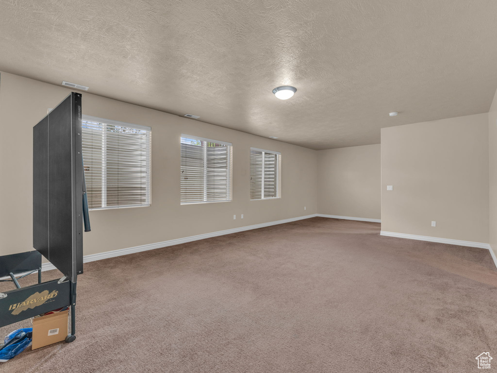 Carpeted empty room featuring a textured ceiling and baseboards