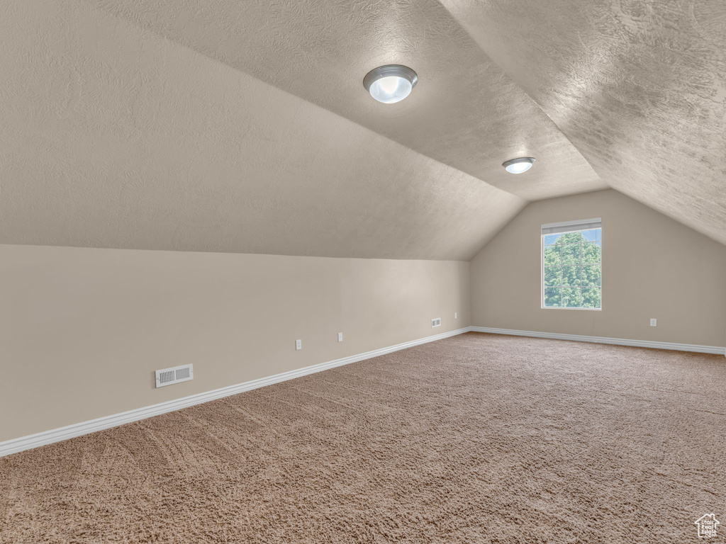 Bonus room with a textured ceiling, baseboards, carpet flooring, and vaulted ceiling